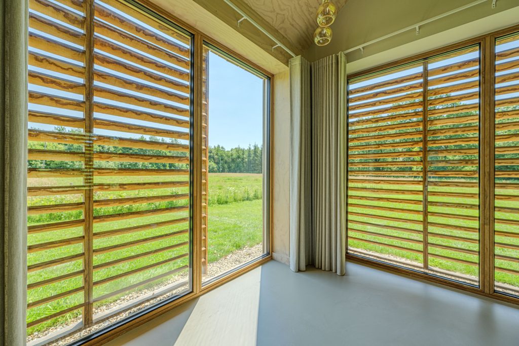Interieurfoto van buitenkozijnen voorzien van houten schuifrekken aan de buitenzijde tegen zoninstraling