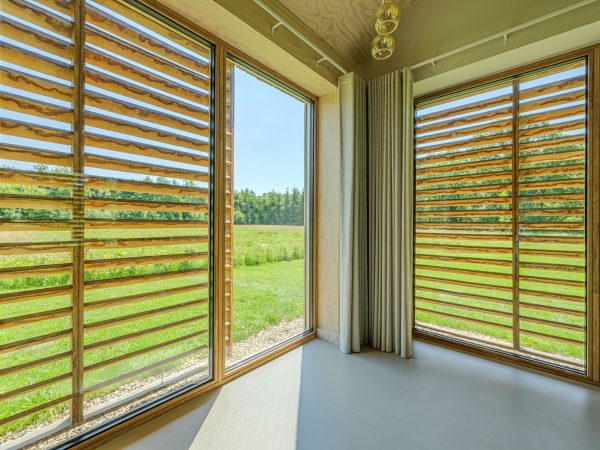 Interieurfoto van buitenkozijnen voorzien van houten schuifrekken aan de buitenzijde tegen zoninstraling